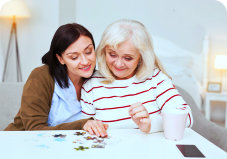 elder woman being assisted by a caregiver in forming a puzzle